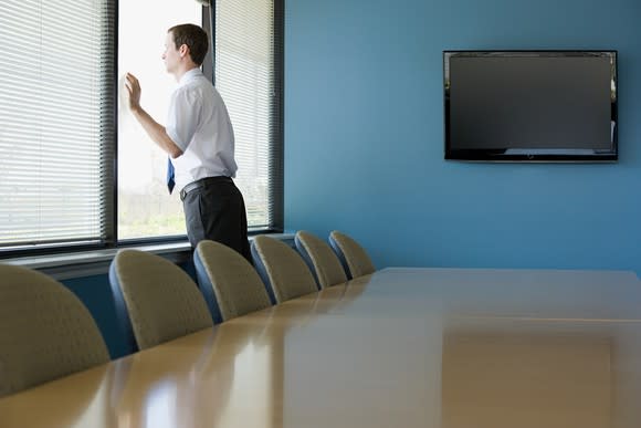 Man in empty conference room standing and looking out the window.