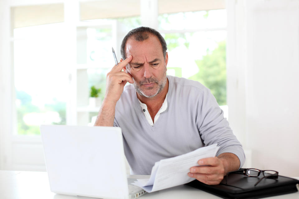 Man sitting in front of a computer looking at papers with concern.