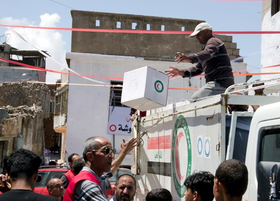 A Red Crescent Society worker passes boxes of food down to a fellow worker in east Mosul, Iraq, May 14, 2018.