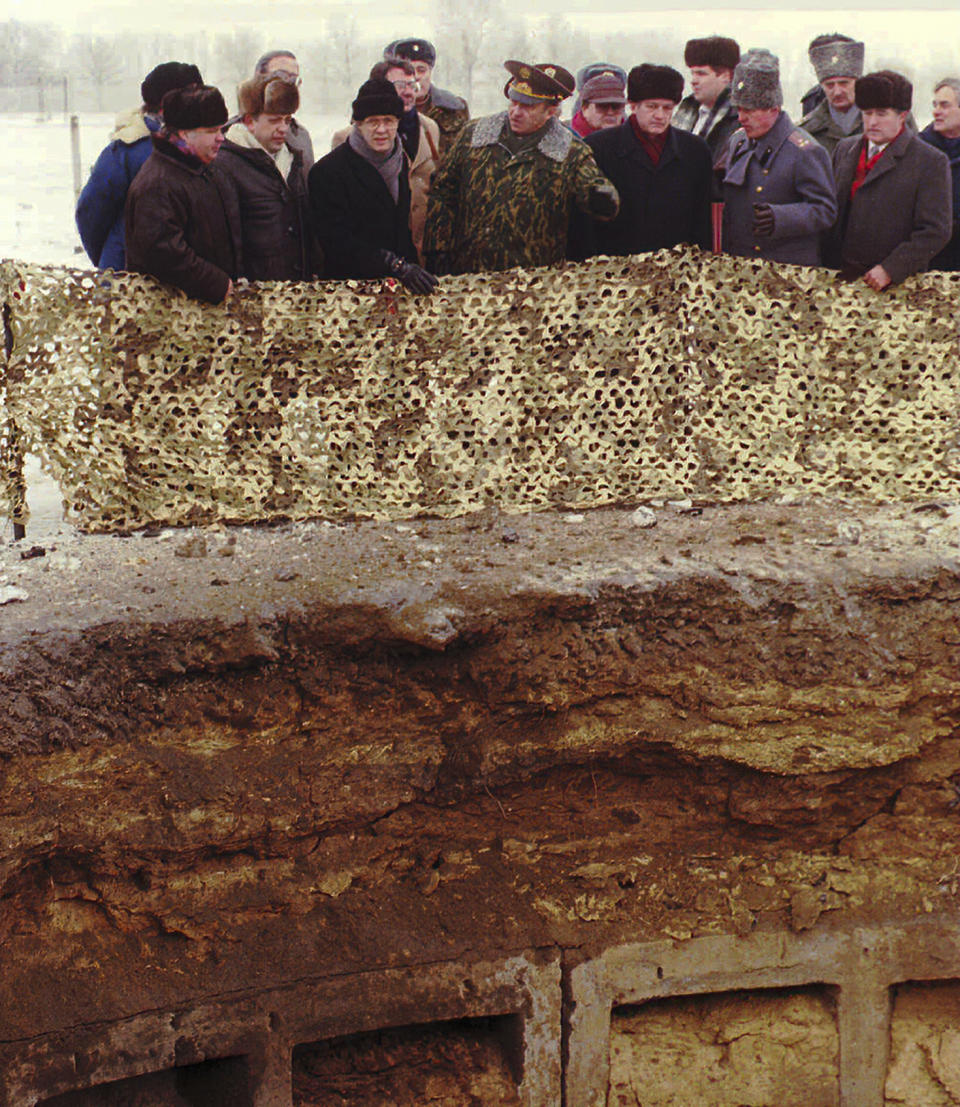 FILE - Secretary of Defense William Perry, third from left, Russian Defense Minister Pavel Grachev, fourth from left, and their Ukrainian counterpart Valery Shmarov, fifth from left, surrounded by military officers of the three countries, stand at the crater of a missile silo that had just been destroyed in a military base near Pervomaysk, some 155 miles south of the Ukraine's capital of Kyiv, on Jan. 5, 1996. With the turn of a key the U.S., Russia and Ukraine defense chiefs put an end to a missile silo that once held nuclear weapons aimed at the United States. (AP Photo/Yefrem Lukatsky, File)