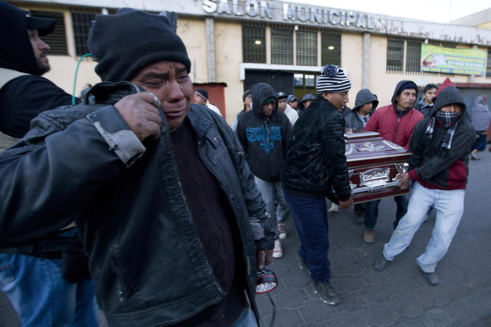 In this March 28, 2019 photo, a resident grieves as a group of men carry away a coffin containing the remains of a victim of a highway accident, in Nahuala, Guatemala. A large truck slammed into a crowd gathered on a dark highway in western Guatemala, killing over a dozen people and leaving bodies scattered on the roadway, firefighters said. Health Minister Carlos Soto said that 18 others, including children, were injured and taken to hospitals. (AP Photo/Sandra Sebastian)