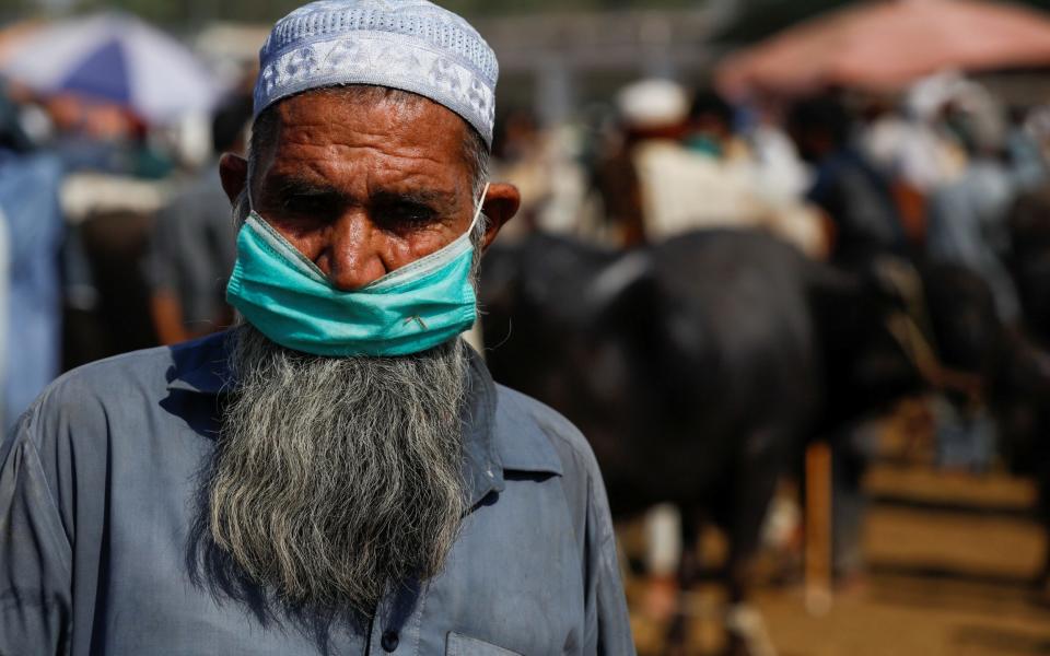 A man wears a protective mask as he sells cows for the upcoming Eid Al Adha sacrifice, at the cattle market, as the spread of the coronavirus disease - Fayaz Aziz/REUTERS