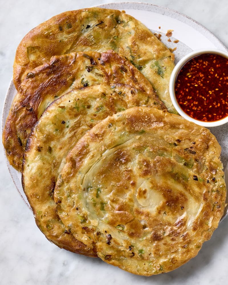 Whole scallion pancakes on a serving platter with a chili dipping sauce.