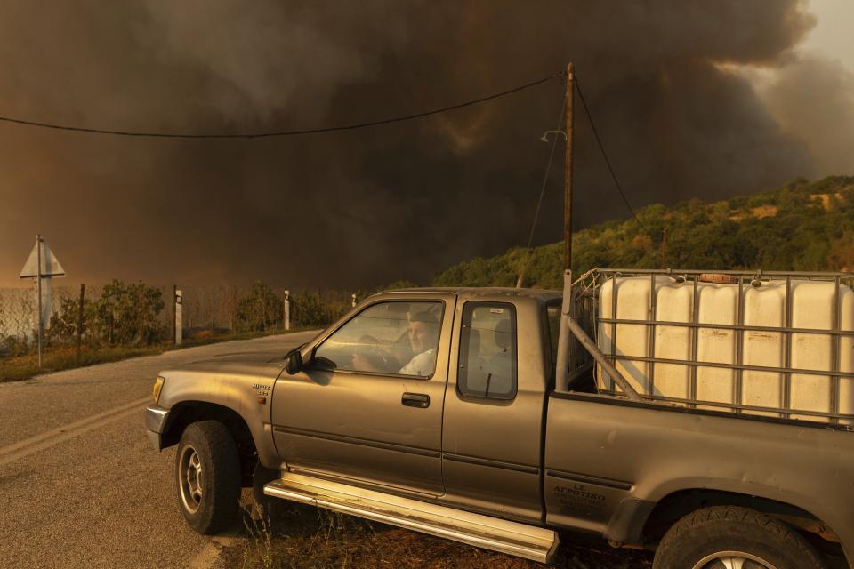 A man drives away as flames burn a forest during wildfires in the village of Sykorrahi, near Alexandroupolis town, in the northeastern Evros region, Greece, Wednesday, Aug. 23, 2023. Advancing flames are devouring forests and homes in Greece as wildfires that have killed 20 people are raging. (AP Photo/Achilleas Chiras)