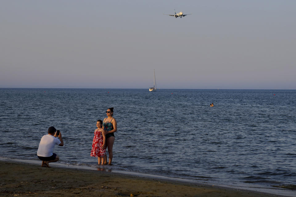 An aircraft prepared for landing at the airport as a tourist family take photos at Makenzi beach in southern coastal city of Larnaca, Cyprus, Monday, May 30, 2022. Hundreds of Russian and Ukrainian Orthodox faithful visiting Cyprus would stream daily past the icon of the Virgin Mary at Kykkos Monastery to venerate the relic that tradition dictates was fashioned by Luke the Evangelist and blessed by the Virgin herself. But a European Union ban on flights to and from Russia as a result of Russia's invasion of Ukraine has meant a loss of 800,000 vacationers - a fifth of all tourists to Cyprus in record-setting 2019. (AP Photo/Petros Karadjias)