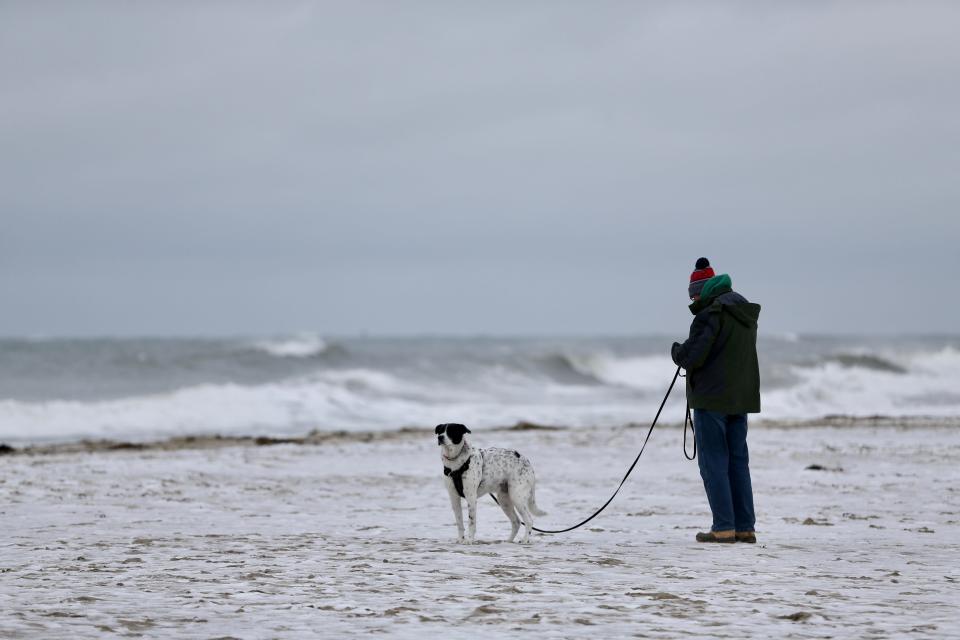 A man walks his dog on snowy Hampton Beach, Monday, Jan. 23, 2023.