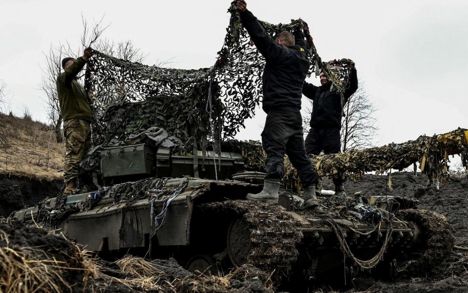 Ukrainian servicemen cover their tank with a camouflage net at a position near a frontline - REUTERS