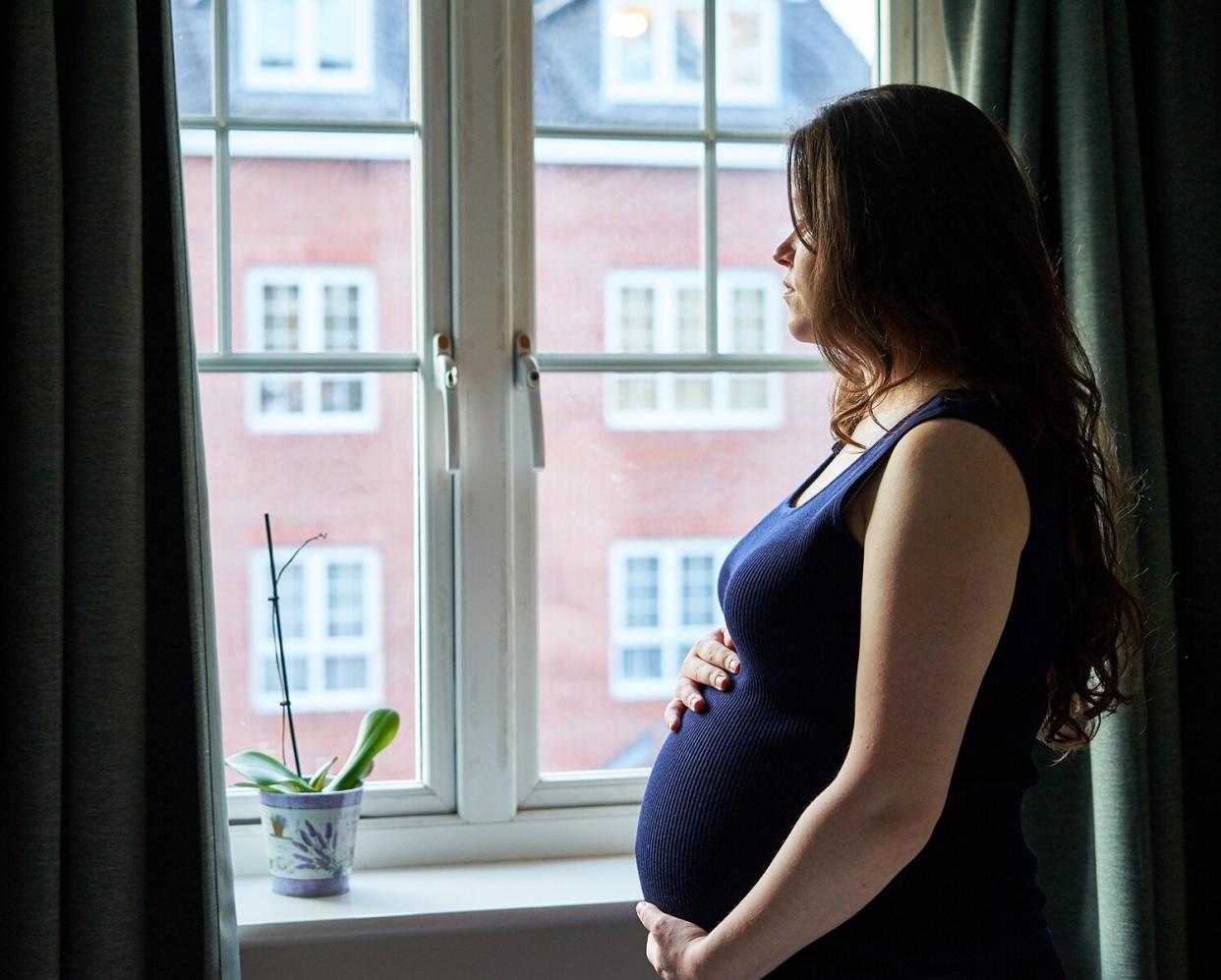 Pregnant Woman Looking Out the Window Holding Belly