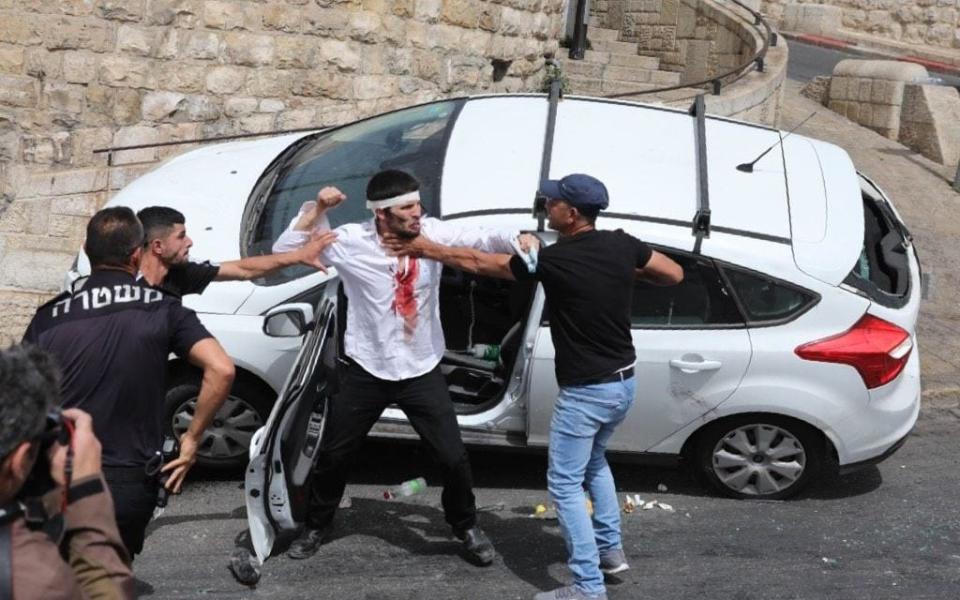 Palestinians scuffle with a wounded Orthodox Jewish man (C) who crashed his car near the Lions' Gate, while police (L) intervene - ABIR SULTAN/Shutterstock