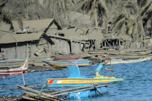 A fisherman paddles his wooden boat next to houses and coconut tress covered in mud and ash due to the eruption of the nearby Taal volcano