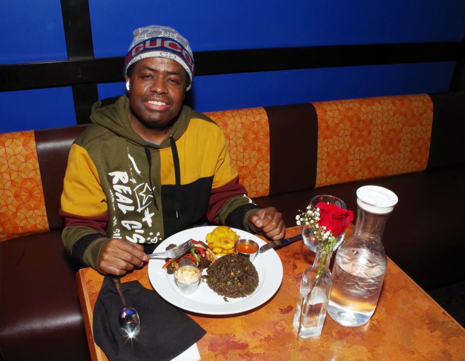 Josh Roberts, who regularly makes the trip to the Tamboo Bistro in Brockton from Melrose to eat, sits down to a dinner of Haitian black rice, fried plantains and fried goat meat on Tuesday, Feb. 15, 2022. He's been coming to Tamboo for 15 years and he says it's worth it.