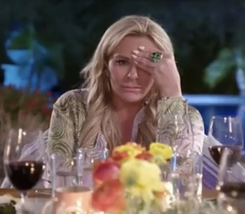 A woman with her hand on her forehead at the dinner table