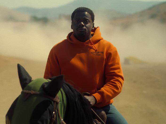 OJ, in an orange hoodie, sits astride black horse Lucky on the Haywood Ranch in this still from &quot;Nope.&quot;