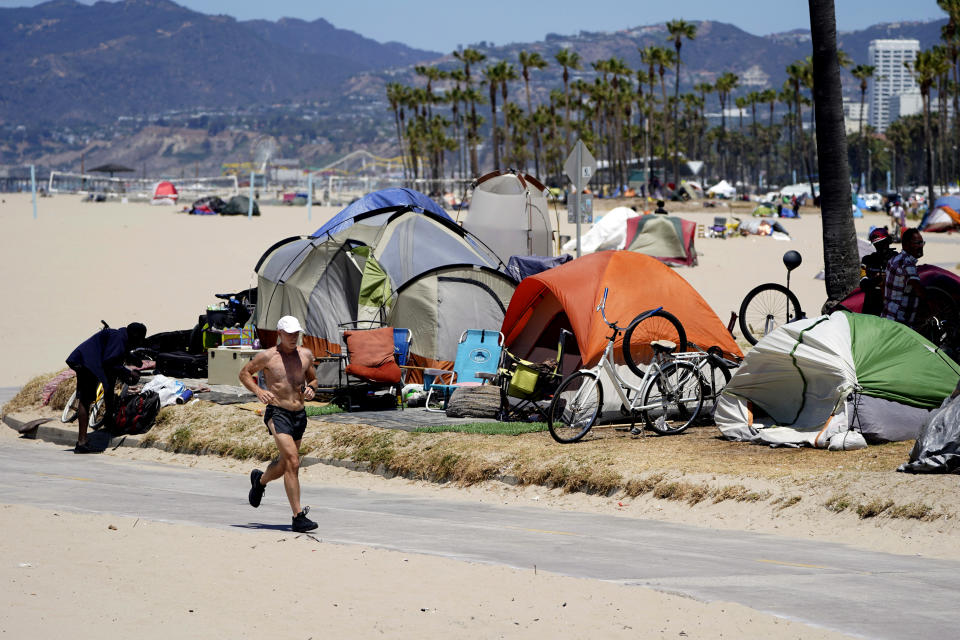 FILE - In this June 8, 2021, file photo, a jogger walks past a homeless encampment in the Venice Beach section of Los Angeles. Los Angeles City Council is poised to clamp down on homeless encampments, making it illegal to pitch tents on some sidewalks, beneath overpasses and near parks. The measure being considered Thursday, July 1, 2021, is billed as a humane way to get people off streets and restore access to public spaces. (AP Photo/Marcio Jose Sanchez, File)