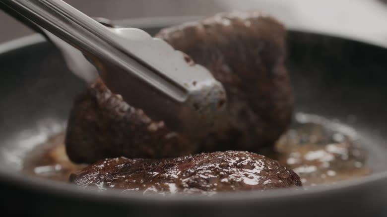 Tongs flipping steak in pan