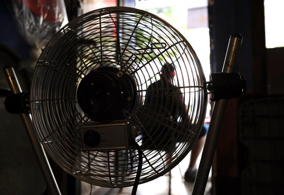 A man sits in the door of a building in Spanish Harlem with a fan running between him and the camera.