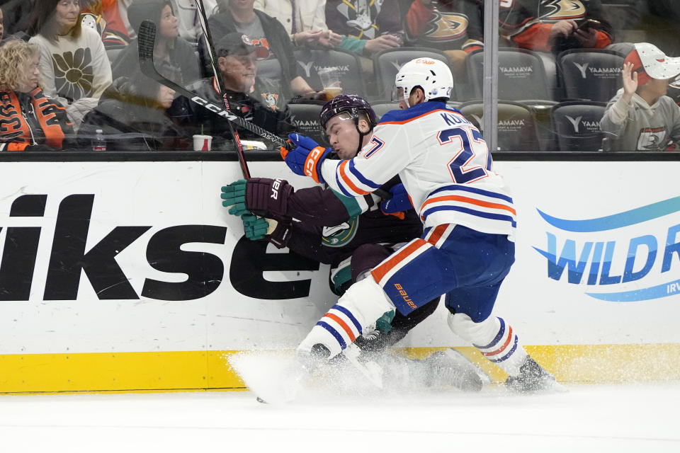 Edmonton Oilers defenseman Brett Kulak, right, puts Anaheim Ducks left wing Ross Johnston into the boards during the first period of an NHL hockey game Sunday, Dec. 31, 2023, in Anaheim, Calif. (AP Photo/Mark J. Terrill)