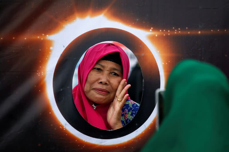 A woman poses for photos behind a banner depicting the solar eclipse during the annular solar eclipse in Siak