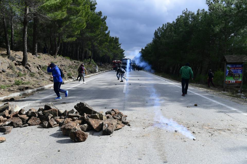 Protesters try to avoid a tear gas canister thrown by riot police during clashes in Karava near the area where the government plans to build a new migrant detention center, on the northeastern Aegean island of Lesbos, Greece, Wednesday, Feb. 26, 2020. Local authorities declared a 24-hour strike on two eastern Greek islands Wednesday to protest government plans to build new migrant detention camps there. (AP Photo/Michael Varaklas)