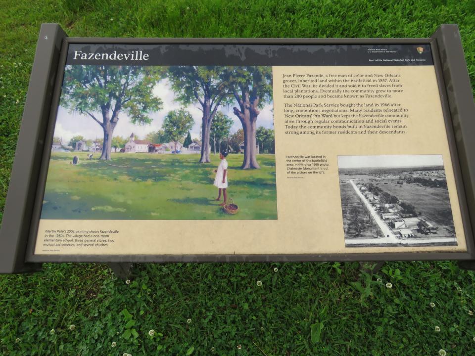 A marker honoring a tiny community founded around 1870 as a place to live for people recently emancipated from slavery stands on Saturday, April 2, 2022, near the road around the fielid where the Battle of New Orleans was fought in 1815. Fazendeville was expropriated in the 1960s to join two sections of a national park. Louisiana iris and African crinum lilies now bloom where the community once stood. (AP Photo/Janet McConnaughey)