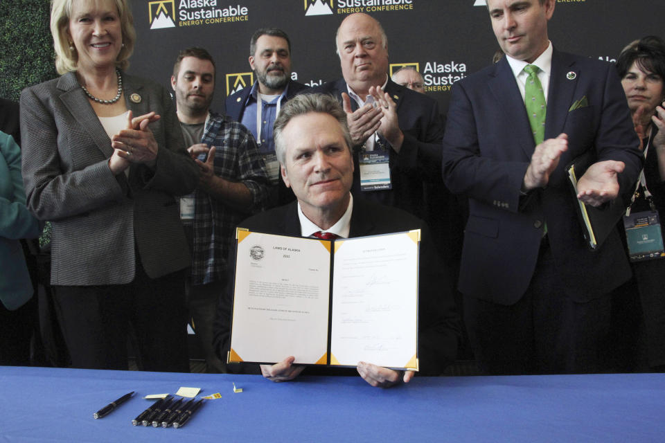 Alaska Gov. Mike Dunleavy displays a bill he had just signed that would allow the state to set up a carbon offset program Tuesday, May 23, 2023, in Anchorage, Alaska. Dunleavy signed the bill with Alaska lawmakers and administration officials standing behind him during the Alaska Sustainable Energy Conference at the Dena'ina Civic and Convention Center in downtown Anchorage. (AP Photo/Mark Thiessen)