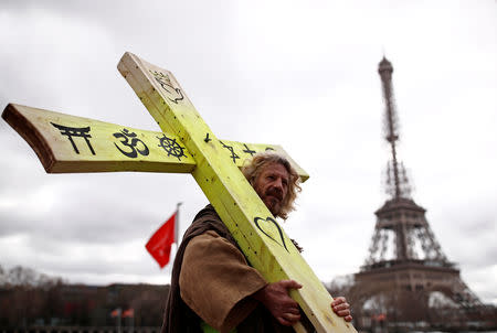 A protester wearing a yellow vest holds a cross as he walks past the Eiffel tower during a demonstration by the "yellow vests" movement in Paris, France, March 2, 2019. REUTERS/Christian Hartmann