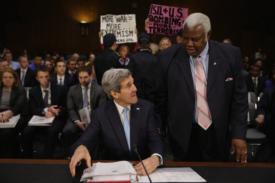 Senate Foreign Relations Committee staffer Bertie Bowman (R) talks with Secretary of State John Kerry before he testifies about a congressional Authorization for the Use of Military Force against the Islamic State, the violent jihadist group that has seized parts of Syria and Iraq, before a hearing in the Dirksen Senate Office Building on Capitol Hill December 9, 2014 in Washington, DC.