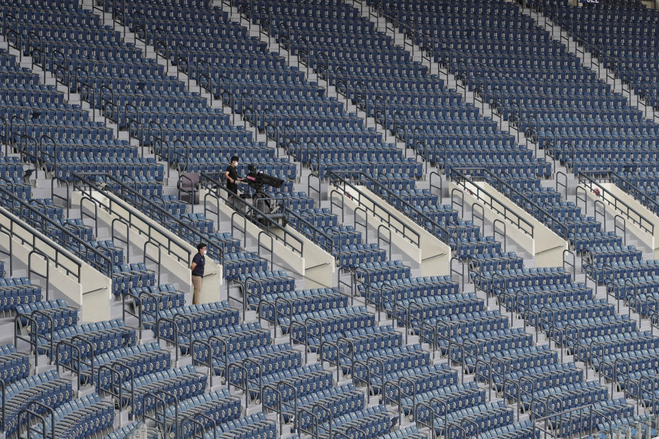 Un cámara de televisión trabaja en medio de filas de asientos vacíos como medida de precaución, durante un juego de la liga KBO de béisbol entre el KT Wiz y los Doosan Bears, en Seúl, Corea del Sur, el domingo 16 de agosto de 2020. (AP Foto/Lee Jin-man)