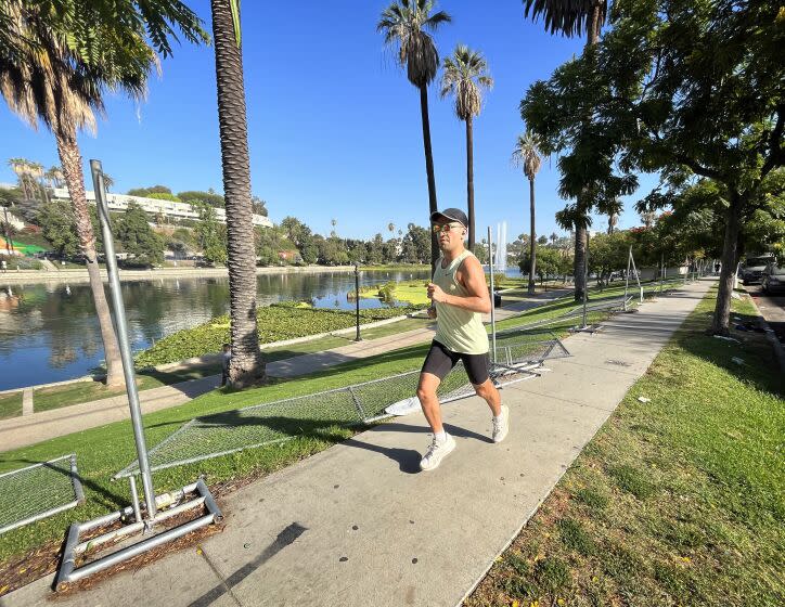 A jogger runs by fencing that was torn down around Echo Park Lake Monday morning, August 8, 2022.