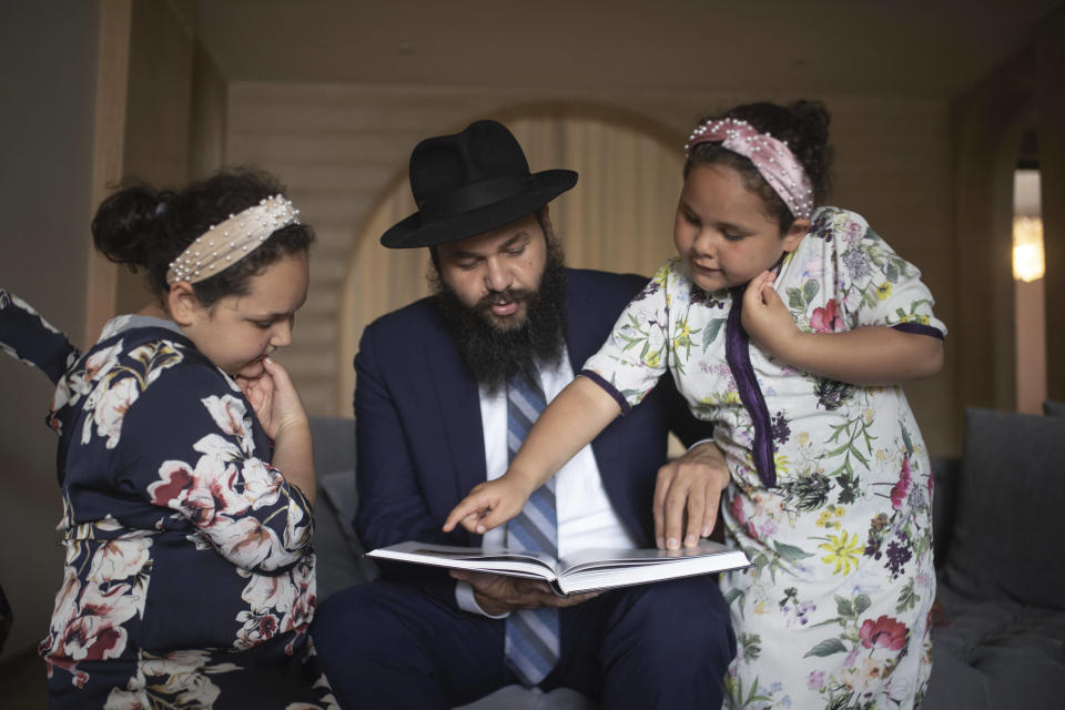 Rabbi Levi Banon and his daughters read a book inside their home in Casablanca, Morocco, Thursday, May 28, 2020. (AP Photo/Mosa'ab Elshamy)