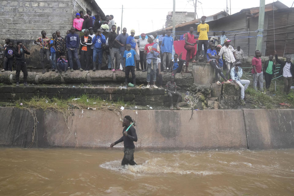 People stand along a river as they watch houses in riparian land being demolished in the Mukuru area of Nairobi, Kenya Tuesday, May. 7, 2024. The government ordered the demolition of structures and buildings, illegally constructed along riparian areas. Kenya, along with other parts of East Africa, has been overwhelmed by flooding. (AP Photo/Brian Inganga)