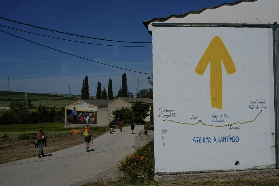 A sign showing the distance to Santiago displayed for pilgrims during a stage of "Camino de Santiago" or St. James Way, in Rabe de la Calzada, northern Spain, Wednesday, June 1, 2022. Over centuries, villages with magnificent artwork were built along the Camino de Santiago, a 500-mile pilgrimage route crossing Spain. Today, Camino travelers are saving those towns from disappearing, rescuing the economy and vitality of hamlets that were steadily losing jobs and population. “The Camino is life,” say villagers along the route. (AP Photo/Alvaro Barrientos)