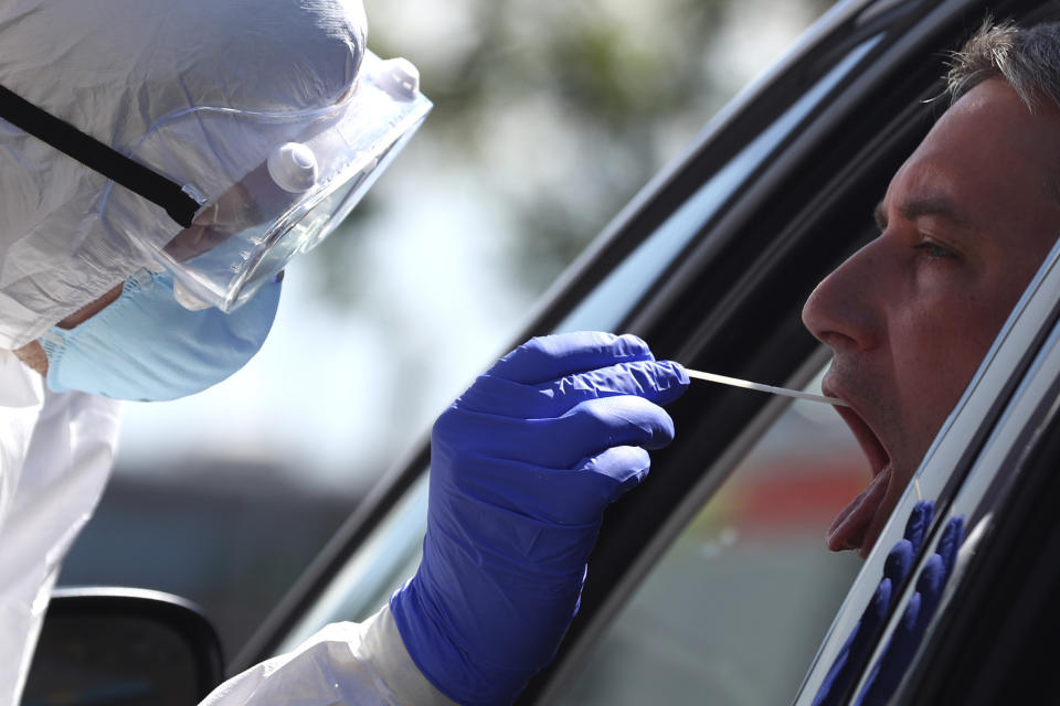 FILE - A medical staff takes a sample for a voluntary coronavirus disease test (COVID-19) at the new corona test station at the 'Hochfelln' service station on the A8 motorway between Salzburg and Munich near Bergen, Germany, July 30, 2020. Germany is set to mark 100,000 deaths from COVID-19 this week, passing a somber milestone that several of its neighbors crossed months ago but which some in Western Europe's most populous nation had hoped to avoid. (AP Photo/Matthias Schrader, File)