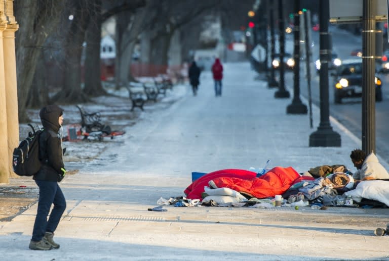 A homeless man, one of about 7,500 in Washington, DC, rests on top of a subway vent grate for warmth as a tourist walks past on January 5, 2018