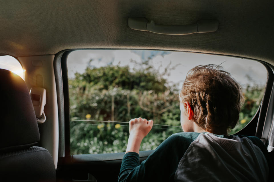 Child looking out car window, landscape visible, sunlight coming through