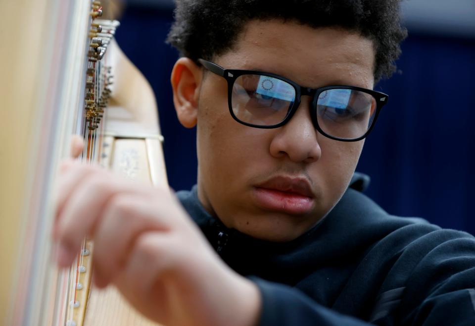 Miles Booker, 14 and a freshman at Cass Technical High School reads the sheet music as he plucks the strings of the harp he is practicing on in Lydia Cleaver's class on Friday, March 24, 2023. Cleaver, the director of the school's harp program and an alum of the school, oversees the students and the thirteen harps as they approach their centennial year of the program.