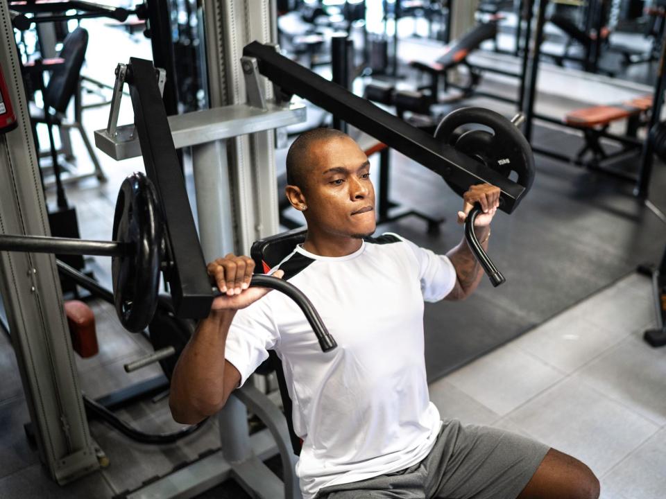 a man in a white T shirt and athletic shorts doing a chest press exercise on a gym machine