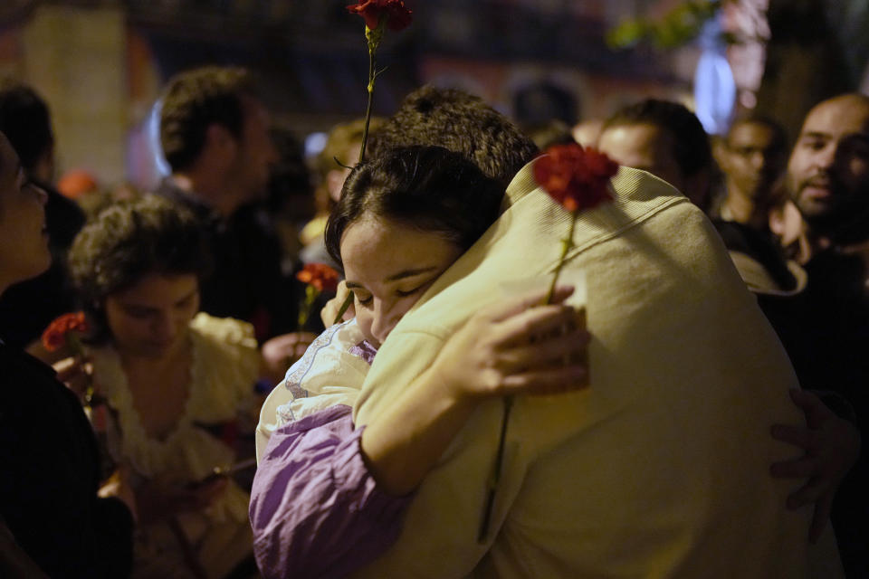 A couple hold red carnations while embracing each other after thousands sang the folk song Grandola, Vila Morena, in the first minutes of Thursday, April 25, 2024, at the Carmo square in Lisbon, as the country celebrates the fiftieth anniversary of the Carnation Revolution. The song by Zeca Afonso was broadcast on national radio as a signal to the troops that the coup was starting and became an icon of the April 25, 1974, revolution that restored democracy in Portugal after 48 years of a fascist dictatorship. (AP Photo/Armando Franca)