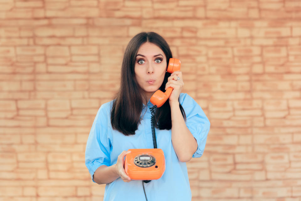 Woman looks surprised while talking on a retro orange telephone