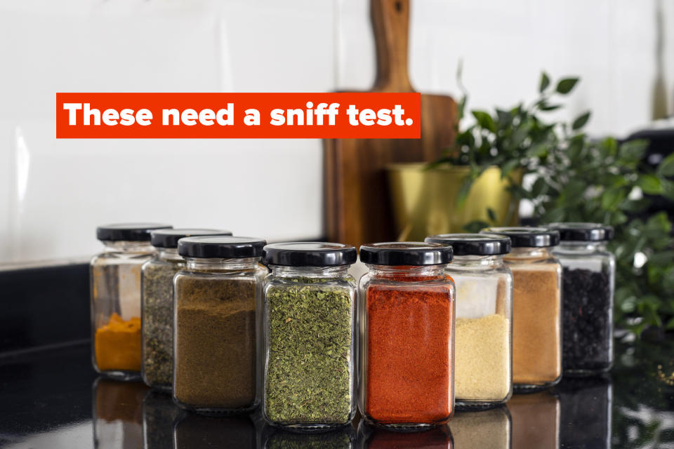 Eight spice jars with various types of herbs inside, displayed on a kitchen counter