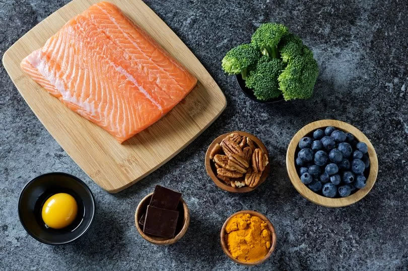 Healthy food including salmon, broccoli, blueberries, nuts, turmeric, dark chocolate, and egg yolk