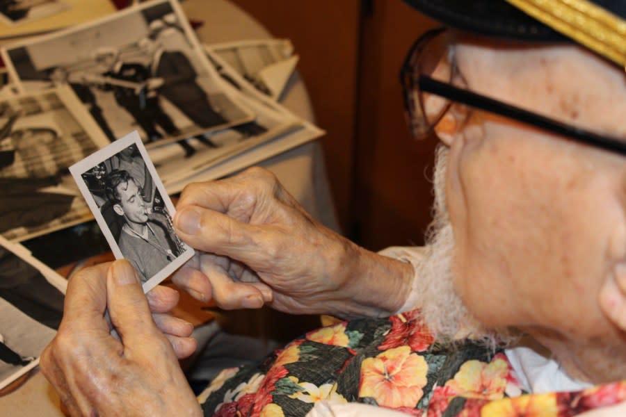 Pearl Harbor survivor Ira “Ike” Schab, 103, looks at an old photo of himself with a saxophone while sitting at the kitchen table in his home in Beaverton, Ore. on Monday, Nov. 20, 2023. Schab was in the U.S. Navy and played tuba in the Navy Band. Eighty-two years later, Schab plans to return to Pearl Harbor on the anniversary of the attack to remember the more than 2,300 servicemen killed. (AP Photo/Claire Rush)