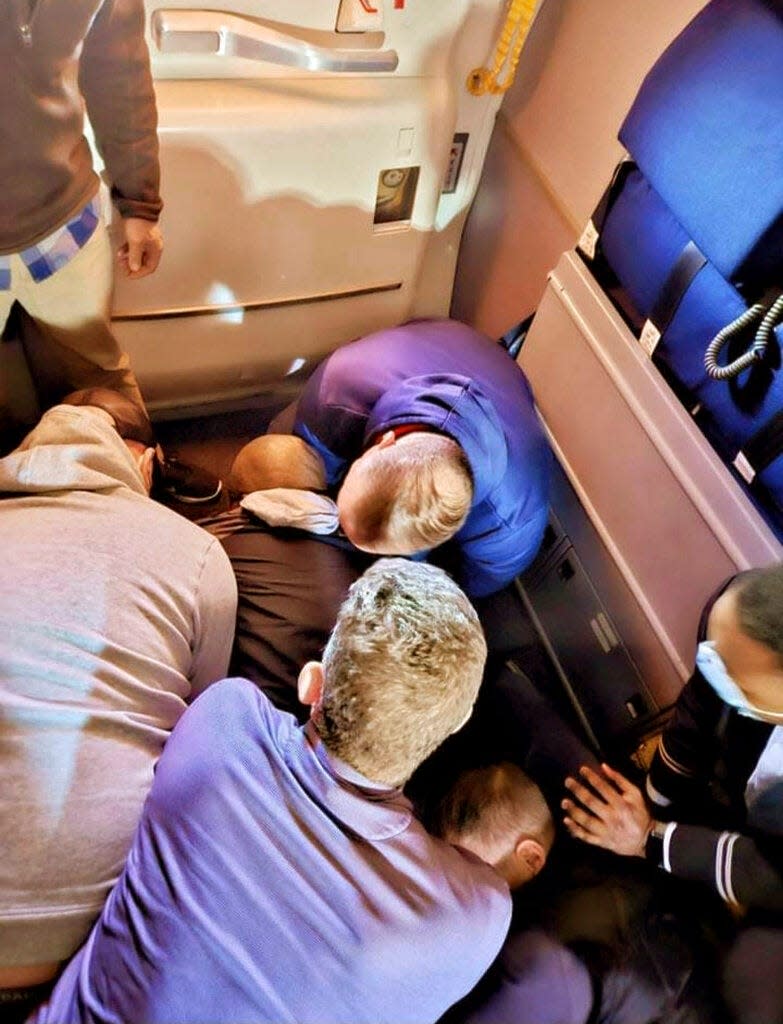 This image provided by Simik Ghookasian shows passengers and crew members restraining a man who according to federal authorities tried to open an airliner’s emergency door and tried to stab a flight attendant on a weekend flight from Los Angeles to Boston Sunday.