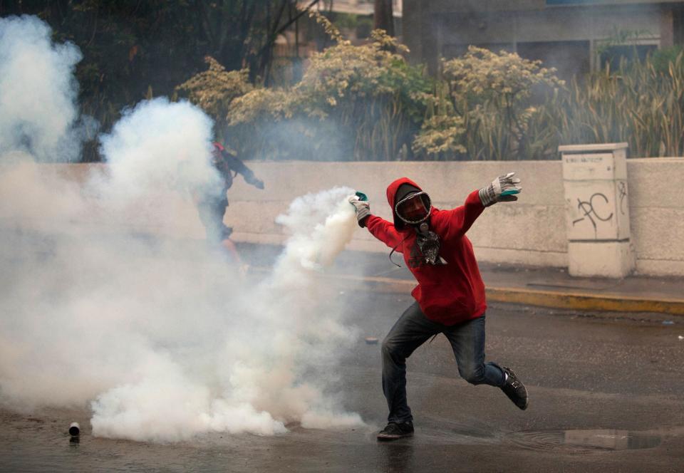 A demonstrator throws back a teargas canister fired by Bolivarian National Police after clashes broke out at an anti-government protest in Caracas, Venezuela, Thursday, May 8, 2014. Demonstrators took to the streets after a pre-dawn raid by security forces that broke up four camps maintained by student protesters and arrested more than 200 people. The tent cities were installed more than a month ago in front of the offices of the United Nations and in better-off neighborhoods in the capital to protest against President Nicolas Maduro's socialist government. (AP Photo/Alejandro Cegarra)