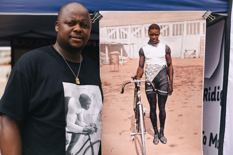 a man stands next to a poster with a portrait of a cyclist