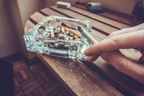 A hand holding a lit cigarette and ashing it into an ashtray.