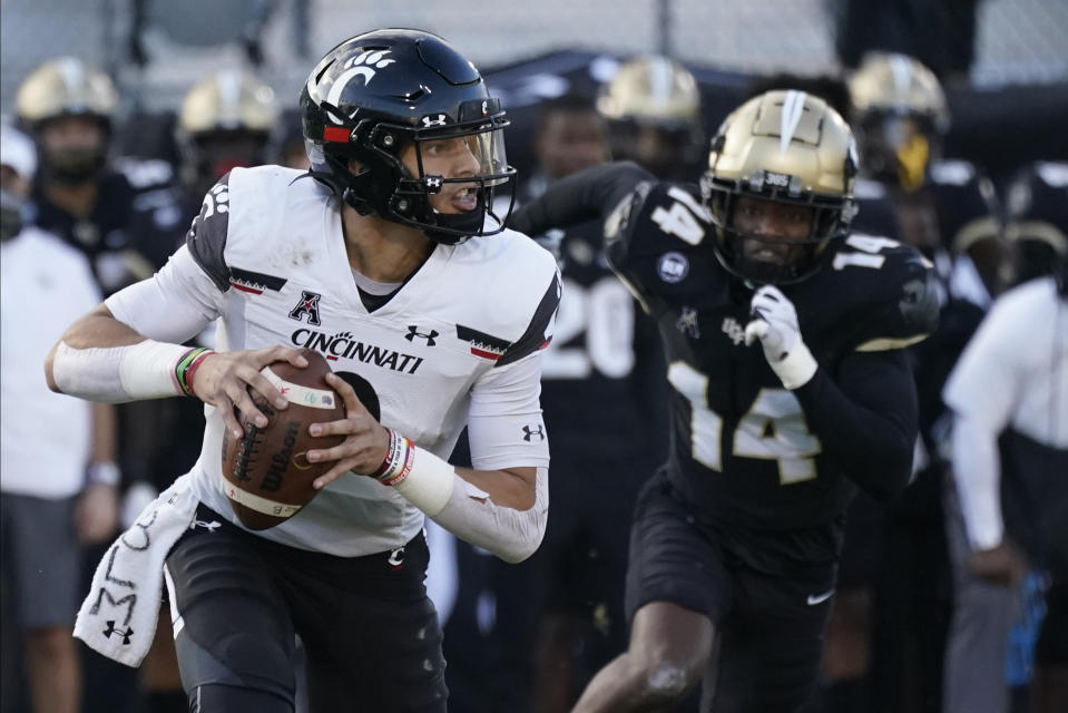 Cincinnati quarterback Desmond Ridder looks for a receiver as Central Florida defensive back Corey Thornton (14) gives chase during the first half of an NCAA college football game, Saturday, Nov. 21, 2020, in Orlando, Fla. (AP Photo/John Raoux)