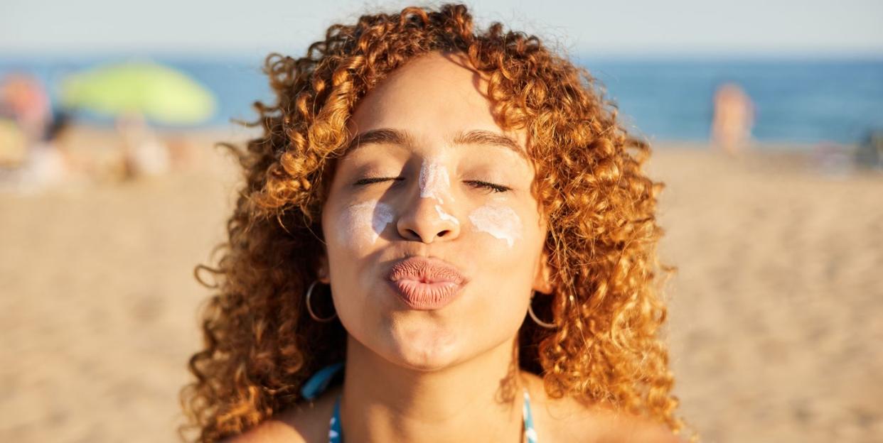 smiling happy woman applying sunscreen to her face on the beach at sunset