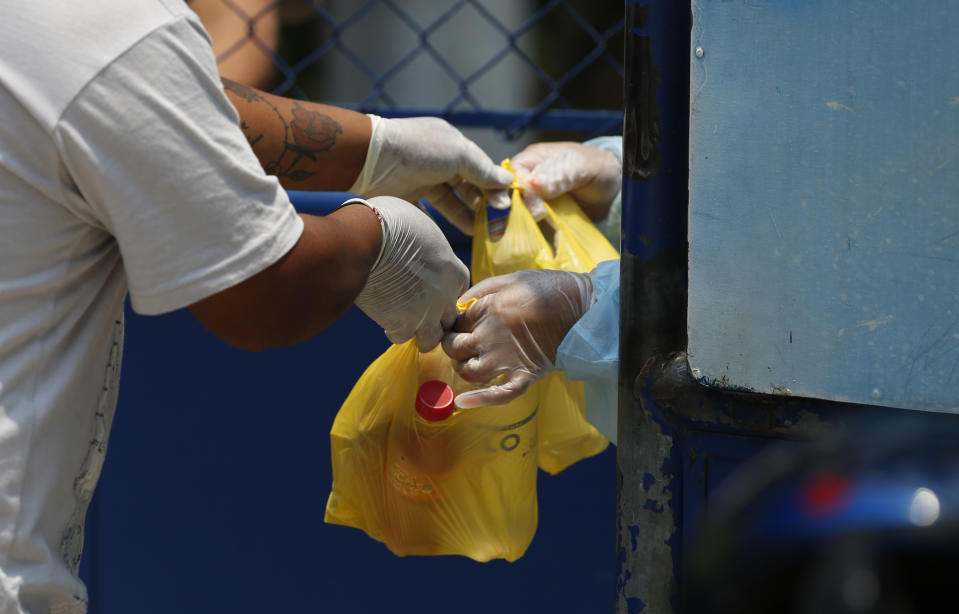 A health worker, right, receives food from a resident, at an athletic dorm facility being used to house Guatemalans deported from the U.S. in Guatemala City, Friday, April 17, 2020. The recently deported Guatemalans were placed here to wait for the results of their tests for the new coronavirus. (AP Photo/Moises Castillo)