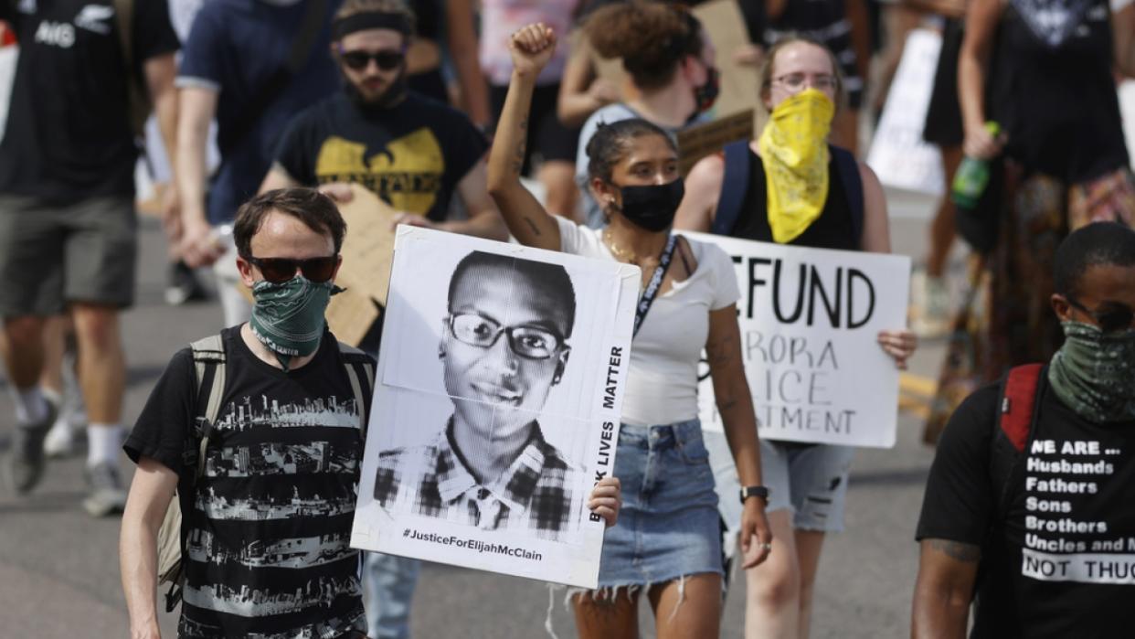 Demonstrators carry placards as they walk down Sable Boulevard during a rally and march over the death of Elijah McClain.